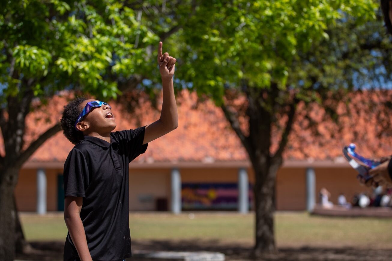 A student smiles and points up at the eclipse.