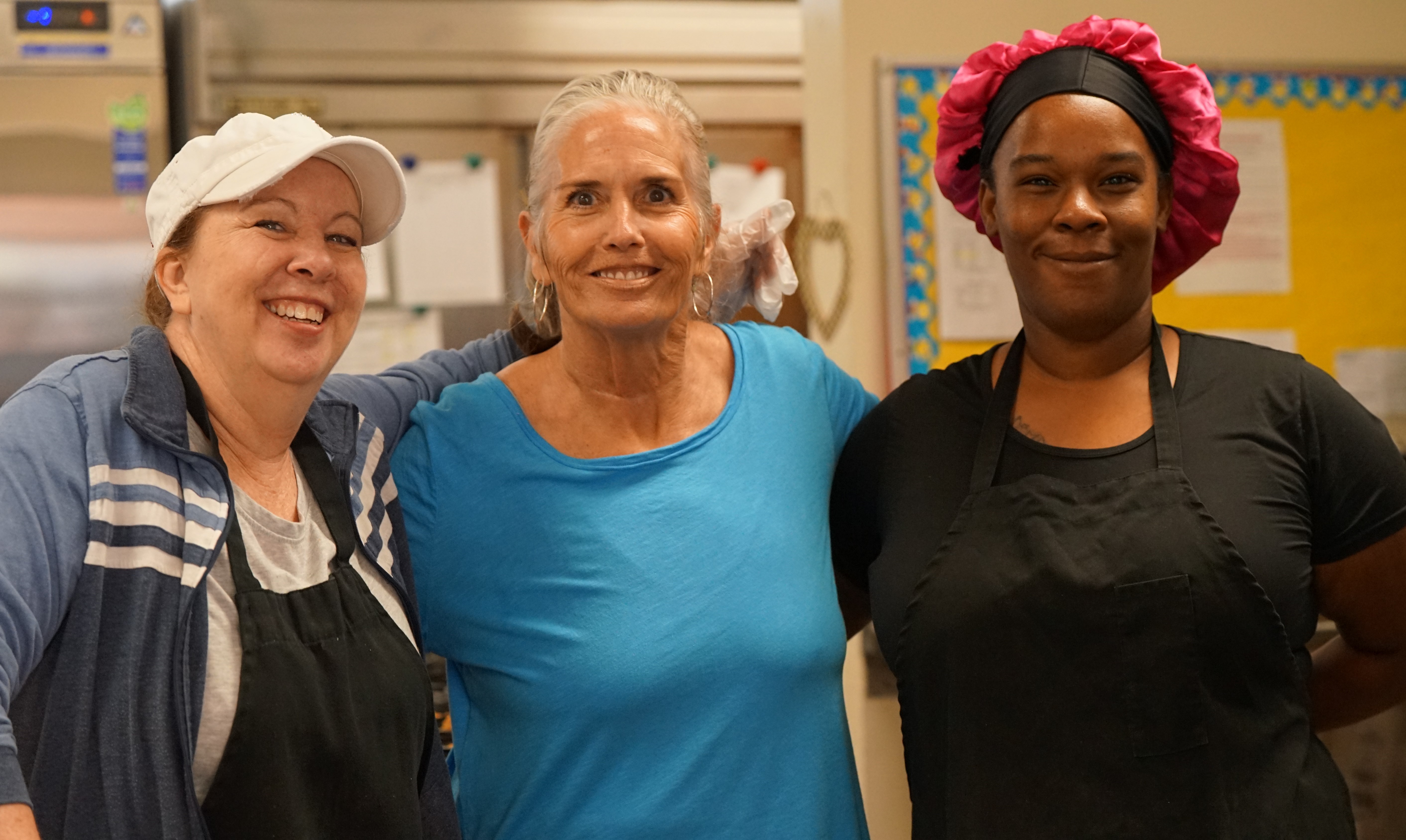 Three cafeteria workers smile on the first day of school