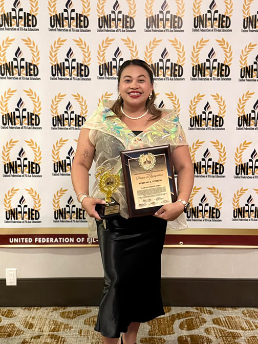 A woman smiles holding an award in front of a backdrop