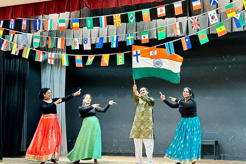 Three women and a man dance on stage holding the Indian flag