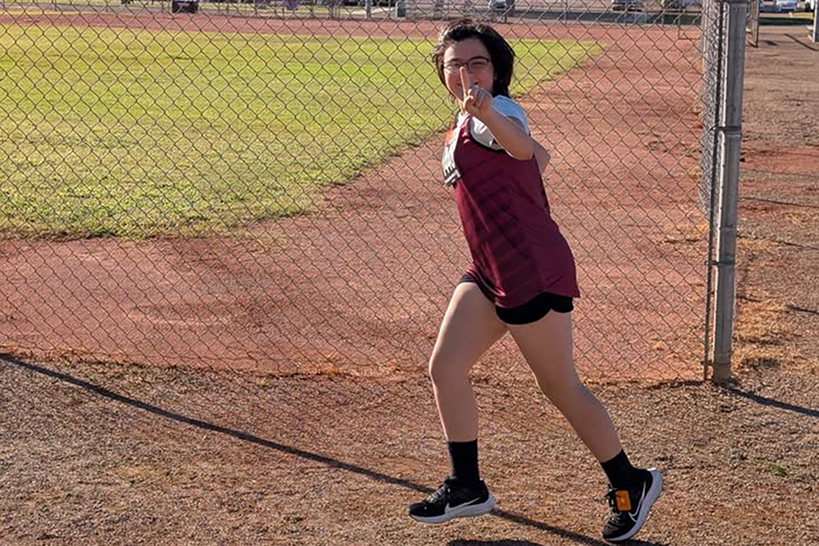 A girl holds up a number 1 finger as she runs around the field