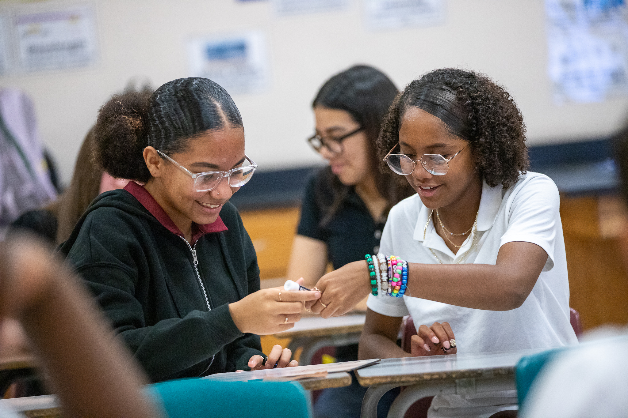 Two teen girls smile as they work on a classroom project together