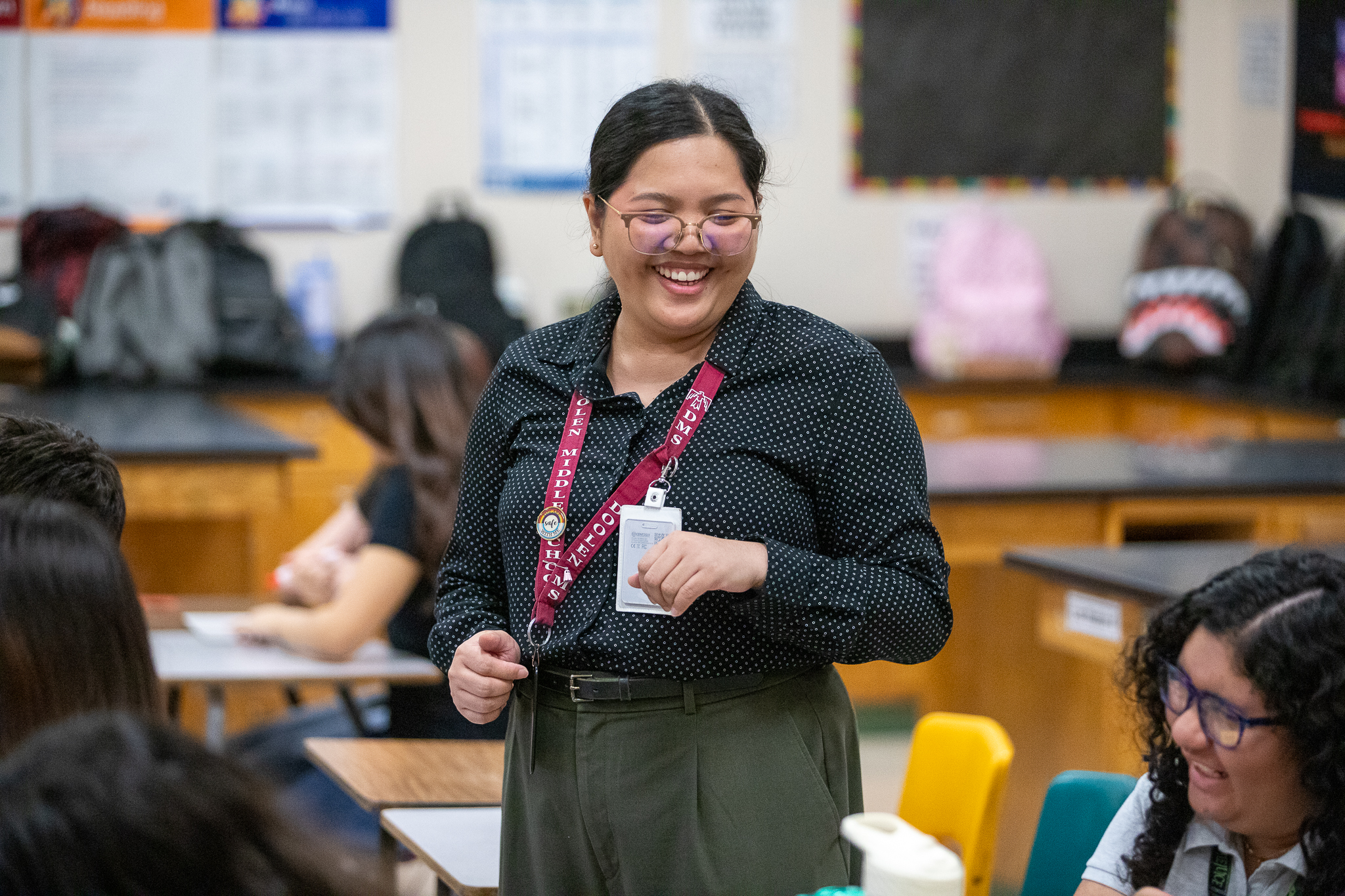 A teacher smiles as she walks through her classroom talking to students