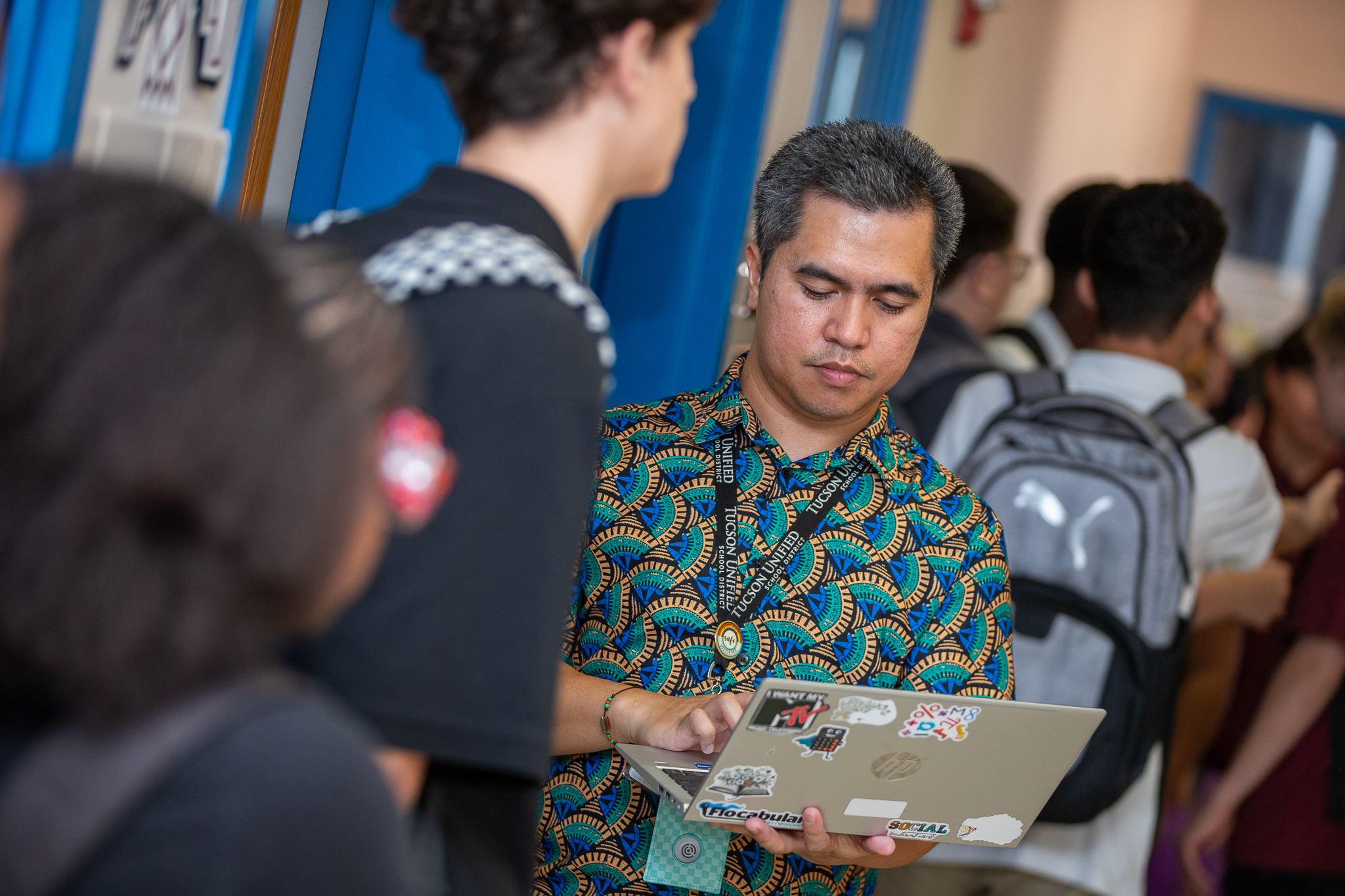 A teacher stands in the hallway working on his laptop between classes
